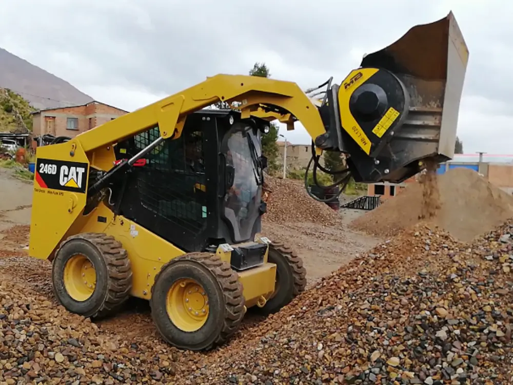 Cargador compacto Caterpillar 246D amarillo con criba/trituradora MB-L170 adjunta, cribando y seleccionando áridos y escombros en una obra. Máquina de Escombros Áridos en acción.