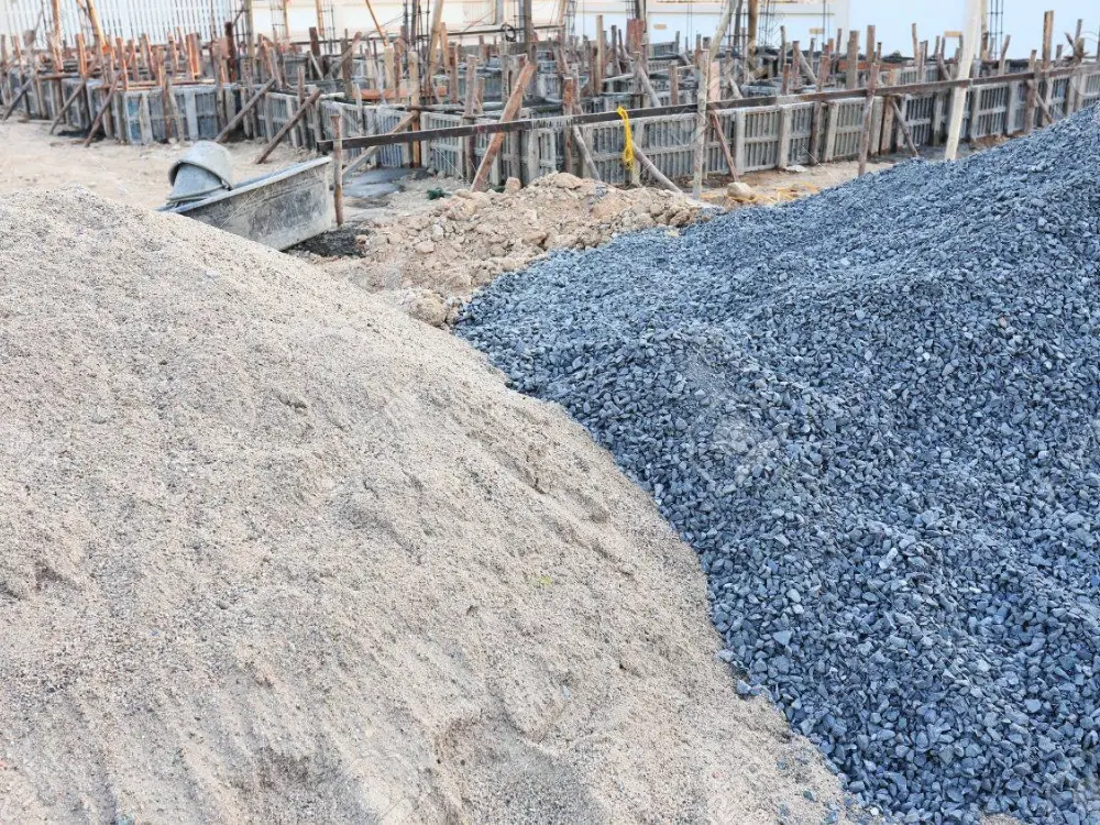 Dos montones, uno de arena y otro de gravilla, entregados por Escombros Áridos en una obra con cimientos en construcción al fondo.