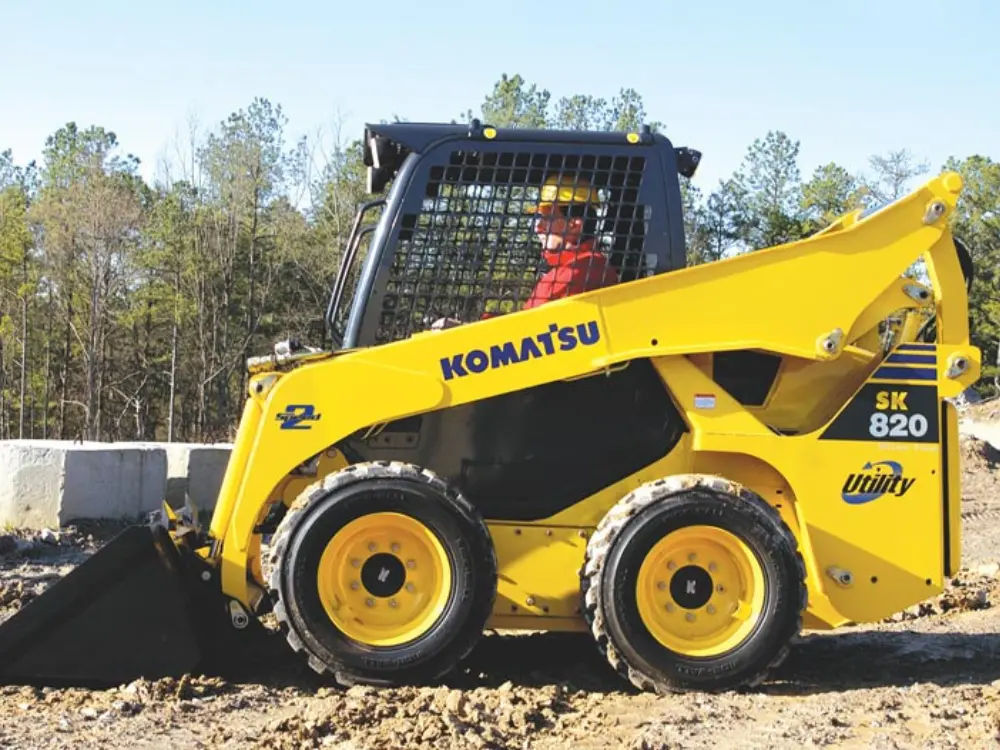 una Mini cargadora Komatsu modelo SK820 de color amarillo utilizada en construcción para carga y retiro de escombros en terreno de obra. de la empresa Escombros Aridos