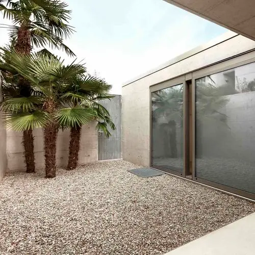 Patio de estilo moderno con suelo de gravilla clara y palmeras, un ejemplo de paisajismo de bajo mantenimiento realizado con áridos de Escombros Áridos.