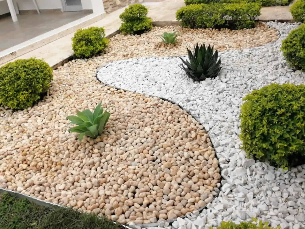 Moderno diseño de paisajismo realizado con los áridos para jardín de Escombros Áridos, combinando piedra blanca y bolones de río para crear un sendero curvo y decorativo.
