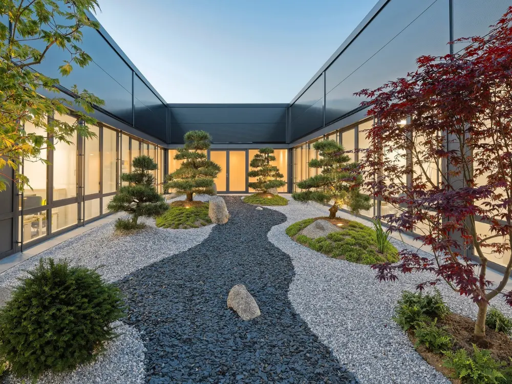 Paisaje de jardín zen con piedras decorativas, plantas ornamentales y árboles alineados, creando un ambiente tranquilo y armonioso. Ideal para espacios modernos con el toque distintivo de Escombros Áridos.