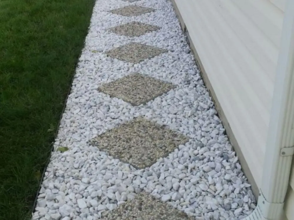 Sendero recto al costado de una casa, construido con grava blanca angular y adoquines de áridos expuestos en forma de rombo.
