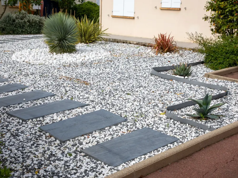 Diseño de xerojardín de Escombros Áridos para un patio delantero, utilizando grava mixta como cubierta, un camino de adoquines de pizarra y una planta de yuca sobre un círculo de canto rodado blanco.