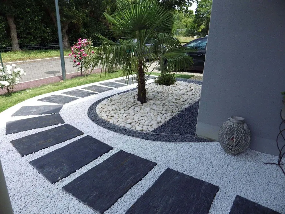 Diseño de acceso moderno de Escombros Áridos, que muestra un sendero de grava blanca con baldosas de pizarra, y una isleta curva con una palmera sobre canto rodado blanco y un borde de gravilla oscura.