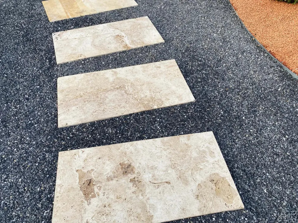 Sendero de jardín con escalones de piedra clara sobre una base de gravilla negra, mostrando el elegante contraste que se logra con los áridos decorativos de Escombros Áridos.