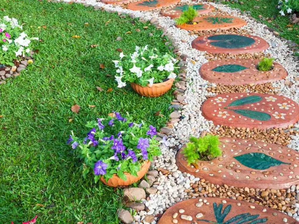 Sendero de jardín decorativo creado con baldosas y grava blanca de Escombros Áridos, rodeado de césped y flores coloridas.