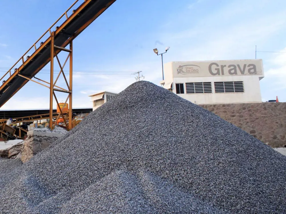 Gran montón de grava para construcción en el patio de la planta de Escombros Áridos, con una cinta transportadora industrial al lado, demostrando nuestra capacidad de abastecimiento.