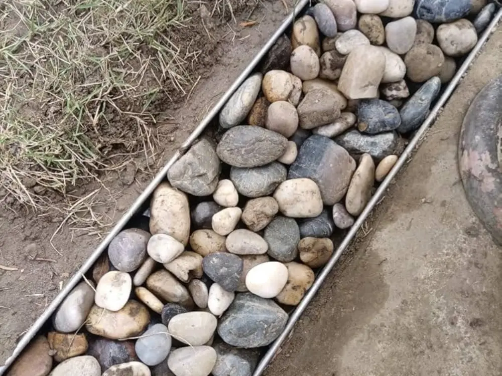 Canal de drenaje decorativo relleno con canto rodado, un producto para paisajismo vendido por Escombro Áridos.