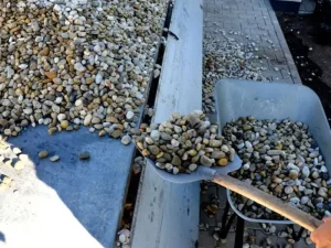 Trabajador cargando grava de río con una pala en una carretilla durante un proyecto de paisajismo, un árido versátil de Escombros Áridos.