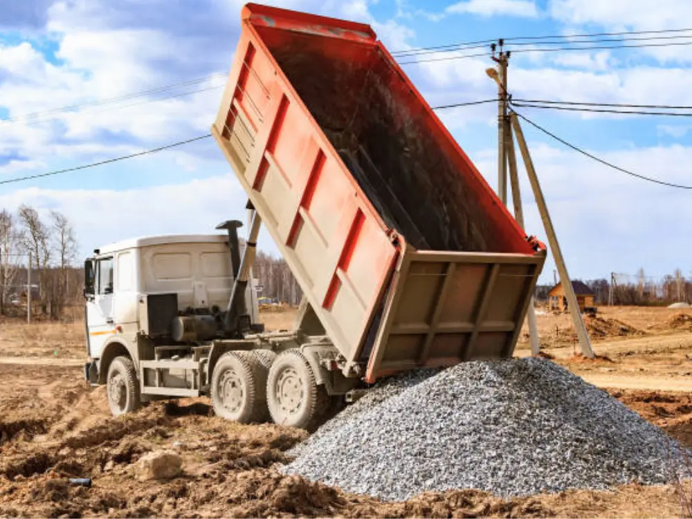 Camión tolva realizando un despacho de áridos, descargando un montón de grava en una obra, servicio ofrecido por Escombros Áridos en Santiago.