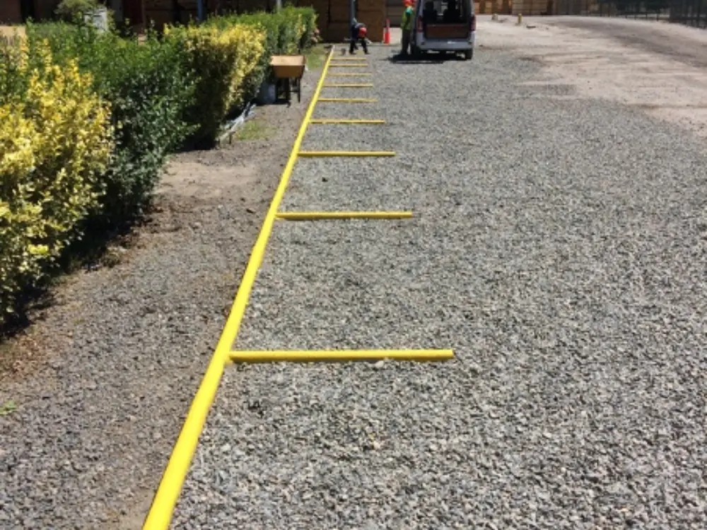 Amplia zona de estacionamiento exterior en un recinto industrial o de acopio, cubierta con gravilla gruesa de color gris oscuro. La imagen muestra la demarcación de un espacio de estacionamiento con tubería o perfiles de plástico de color amarillo brillante. Esta aplicación de árido de Escombro Áridos proporciona una base resistente y económica para áreas de alto tránsito vehicular.
