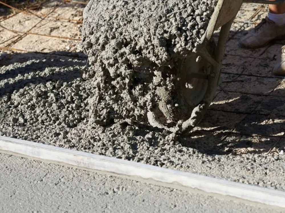 Primer plano de una carretilla vertiendo hormigón (que contiene gravilla como agregado) sobre una malla de acero. La gravilla es esencial para crear una base sólida y durable, material disponible en Escombros Áridos.