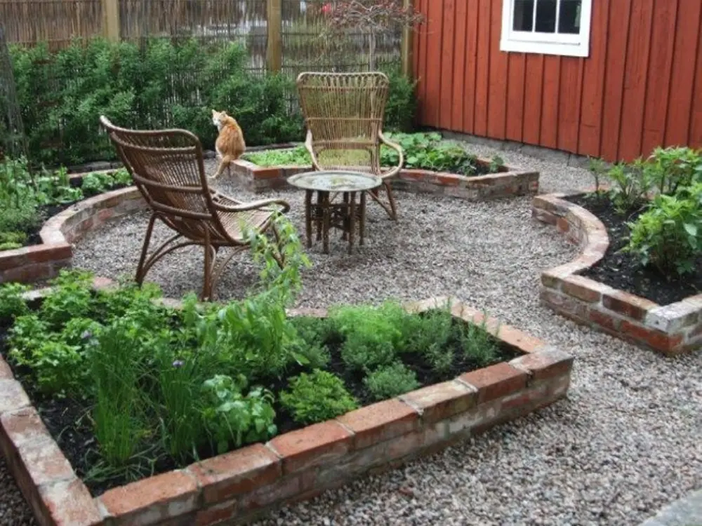Diseño de patio con gravilla en el suelo, rodeado de jardineras elevadas de ladrillo y asientos de mimbre. Crea un espacio de descanso y relajación. Escombros Áridos provee gravilla para paisajismo y decoración de jardines.