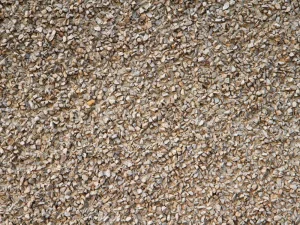 Primer plano de revestimiento de muro con textura de gravilla color café claro, utilizado en estucos o fachadas. Áridos de calidad para acabados de construcción de Escombros Áridos en Santiago.