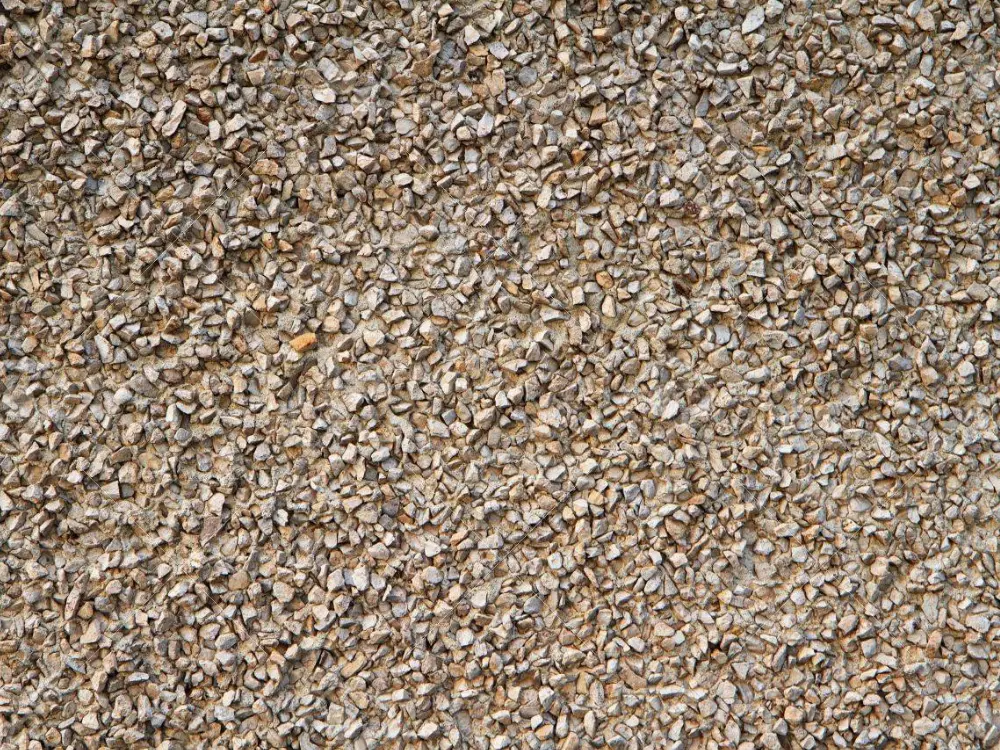 Primer plano de revestimiento de muro con textura de gravilla color café claro, utilizado en estucos o fachadas. Áridos de calidad para acabados de construcción de Escombros Áridos en Santiago.