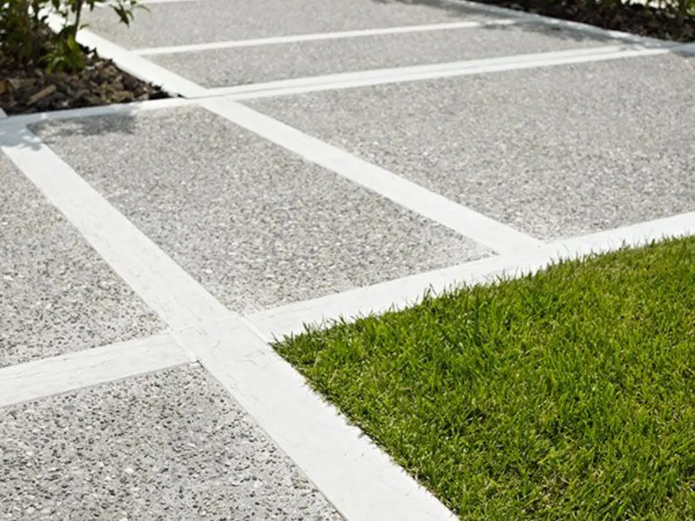 Diseño moderno de camino exterior con hormigón de árido expuesto y separadores blancos, ideal para patios y paisajismo. La gravilla de calidad para este acabado está disponible en Escombros Áridos.