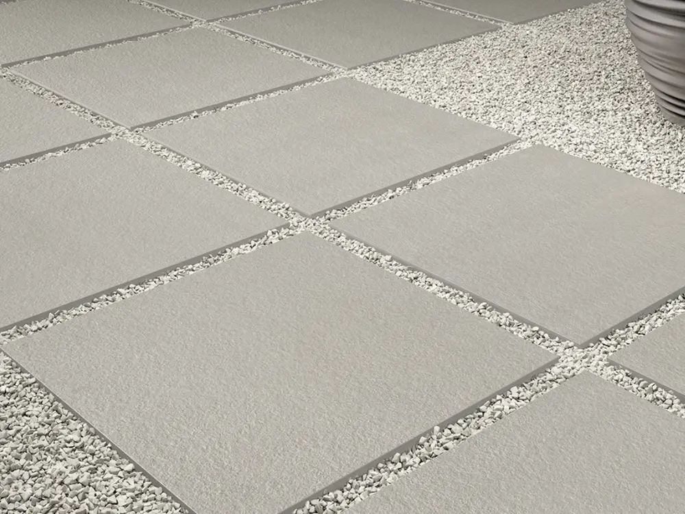 Diseño moderno de piso exterior con baldosas cuadradas y juntas rellenas con gravilla fina, utilizada para drenaje eficiente y estética. Gravilla de alta calidad disponible en Escombros Áridos.