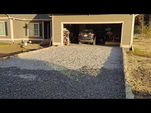 Amplia toma de una entrada de garaje en una casa residencial, cubierta con una capa de grava gruesa de color gris. La grava ha sido contenida con un bordillo de piedra para delimitar el acceso. Esta aplicación demuestra un uso práctico y económico de los áridos de Escombro Áridos para crear una superficie de entrada vehicular drenante y duradera.