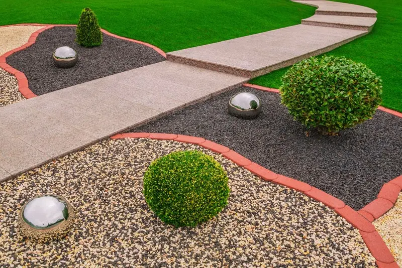 Paisajismo moderno con áreas de gravilla negra y multicolor, separadas por un camino de baldosas, un ejemplo del acabado profesional que se logra con los áridos de Escombros Áridos.