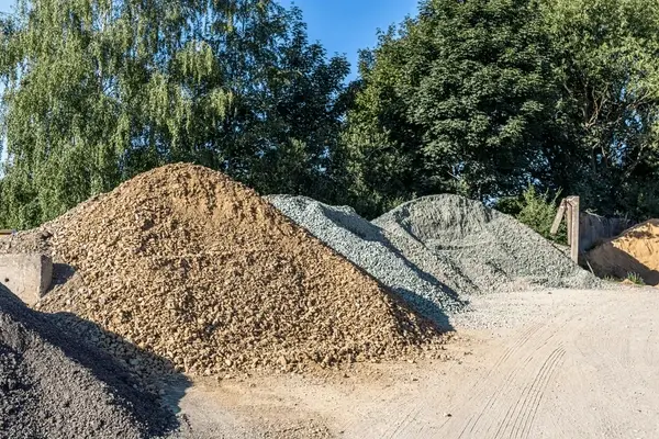 Diversas pilas de áridos, incluyendo grava de color café y gris, y arena, disponibles para la venta en el patio de Escombros Áridos.