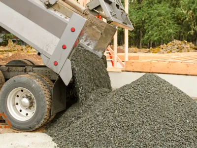Camión volquete descargando una gran pila de gravilla en un sitio de construcción. Se observa el material grueso y oscuro. Escombros Áridos ofrece venta de gravilla con despacho para grandes proyectos.