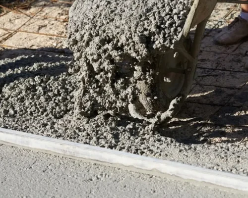 Primer plano de una carretilla vertiendo hormigón (que contiene gravilla como agregado) sobre una malla de acero. La gravilla es esencial para crear una base sólida y durable, material disponible en Escombros Áridos.