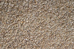 Primer plano de revestimiento de muro con textura de gravilla color café claro, utilizado en estucos o fachadas. Áridos de calidad para acabados de construcción de Escombros Áridos en Santiago.