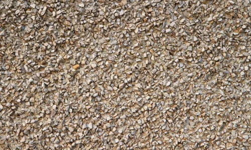 Primer plano de revestimiento de muro con textura de gravilla color café claro, utilizado en estucos o fachadas. Áridos de calidad para acabados de construcción de Escombros Áridos en Santiago.