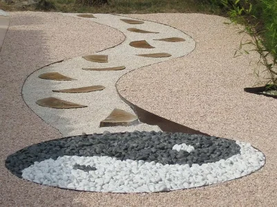 Jardín decorativo con sendero curvo de gravilla blanca y rosa, complementado con un diseño Yin Yang de piedras blancas y grises, destacando la versatilidad de los productos de Escombros Áridos.