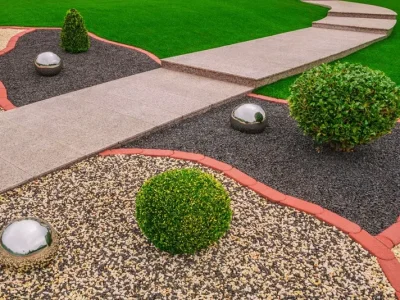 Paisajismo moderno con áreas de gravilla negra y multicolor, separadas por un camino de baldosas, un ejemplo del acabado profesional que se logra con los áridos de Escombros Áridos.
