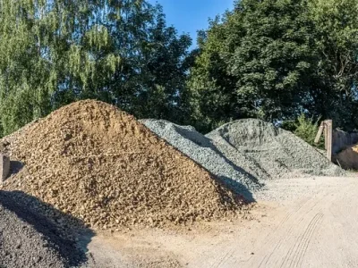 Diversas pilas de áridos, incluyendo grava de color café y gris, y arena, disponibles para la venta en el patio de Escombros Áridos.